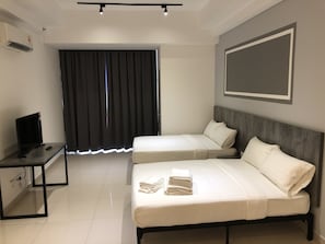 A hotel room with two beds, a desk with a TV, and a large window with curtains.