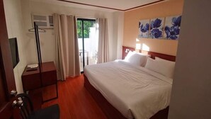 Quarto de hotel com cama, escrivaninha, cadeira e janela com cortinas.