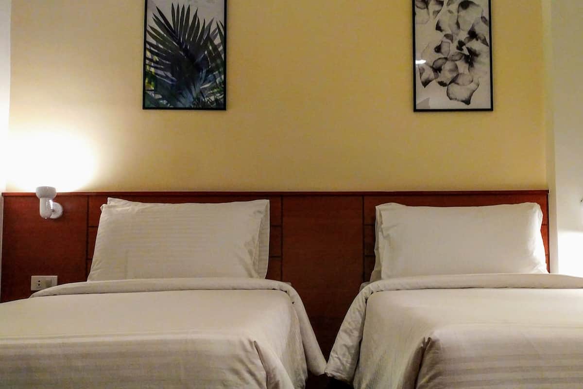 Une chambre d’hôtel avec deux lits, une tête de lit en bois et deux appliques murales.