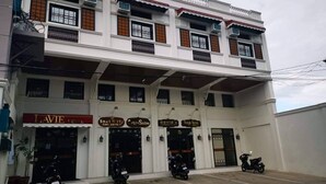 Um edifício de dois andares com diversos estabelecimentos comerciais no andar térreo, incluindo um hotel, uma agência de viagens e um restaurante de sushi.