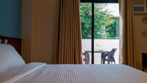 Quarto de hotel com cama, cortinas e vista para área externa com mesa e cadeiras.