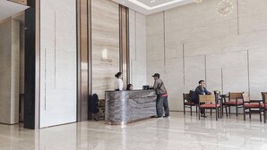 A modern hotel reception area with a marble reception desk, a receptionist, and a guest area with seating.