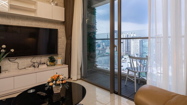 A modern living room with a large flat-screen TV, a coffee table with flowers, a sofa, and a view of a cityscape through a glass door.
