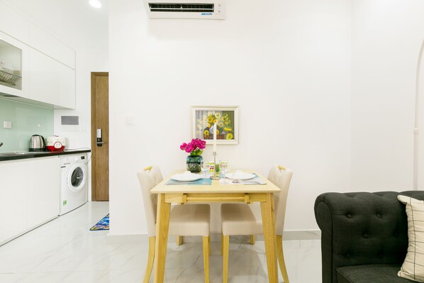 A compact kitchen with a washing machine, a dining table with chairs, and a black sofa. - Justay Sunrise City (Ho Chi Minh City)