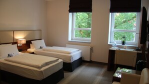 Habitación de hotel con dos camas, un escritorio, una silla y ventana con vistas a árboles.