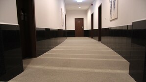 Un pasillo con alfombra, una puerta con el número 112 y un cuadro en la pared.