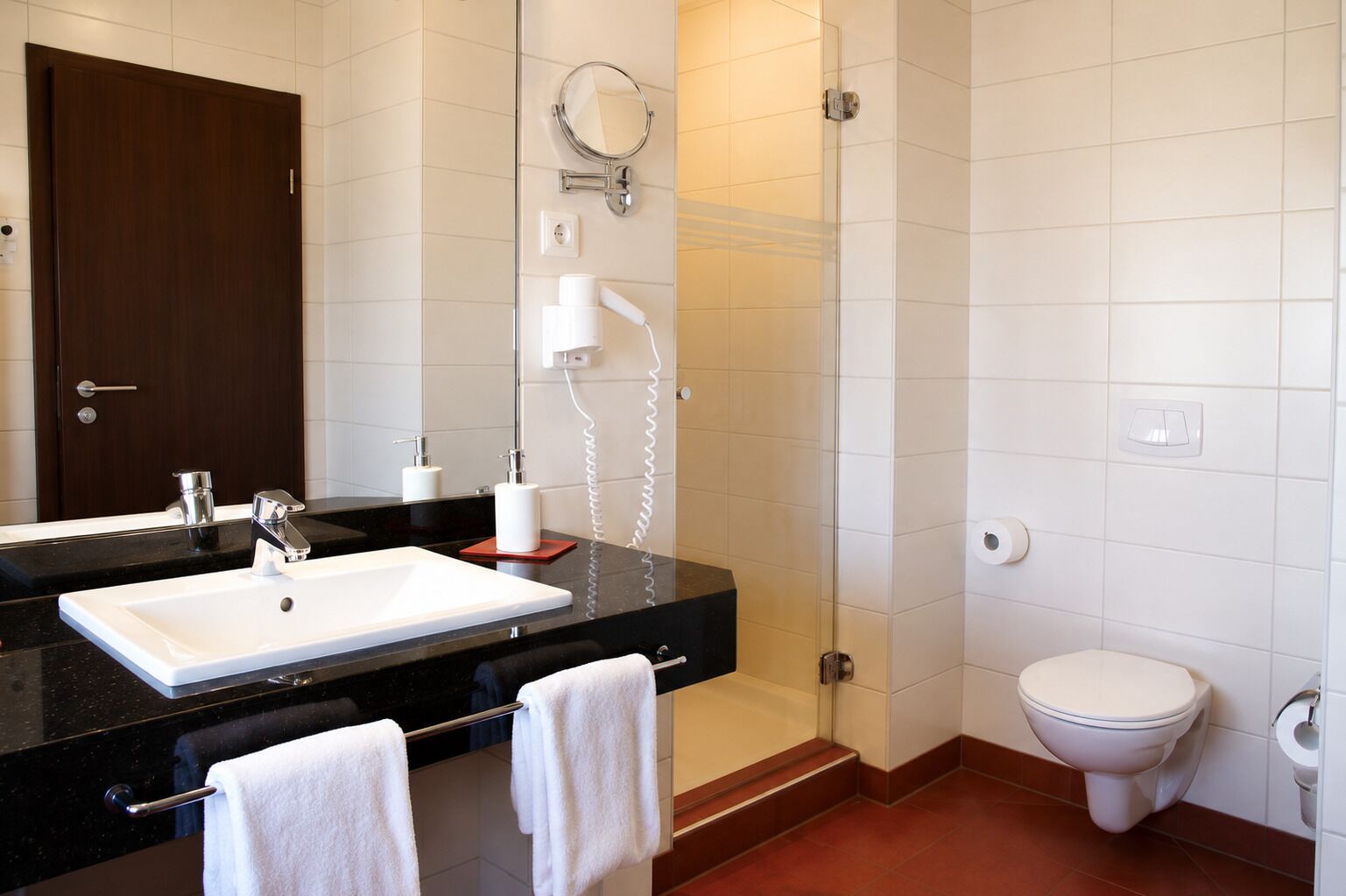 A bathroom with a black countertop sink, a mirror, a toilet, and a shower area.