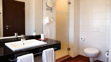A bathroom with a black countertop sink, a mirror, a toilet, and a shower area.