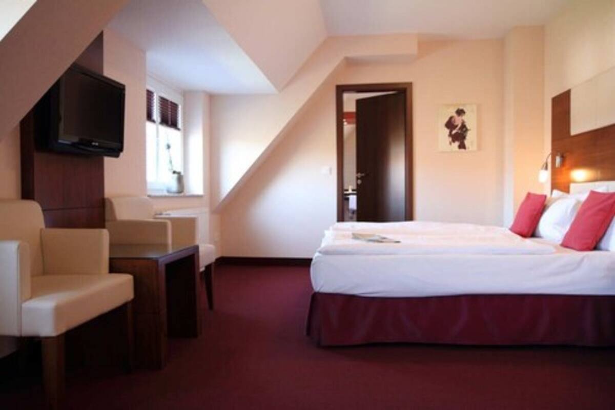 Quarto de hotel com uma cama, televisão fixada na parede e um espaço de estar com cadeiras.