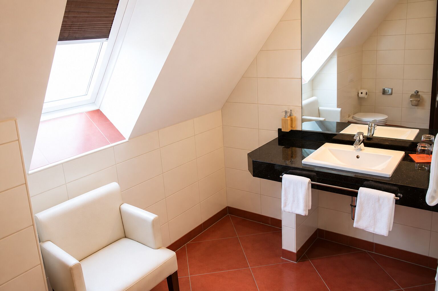 Un baño moderno con tragaluz, una bañera blanca, un lavabo con encimera negra y un espejo.