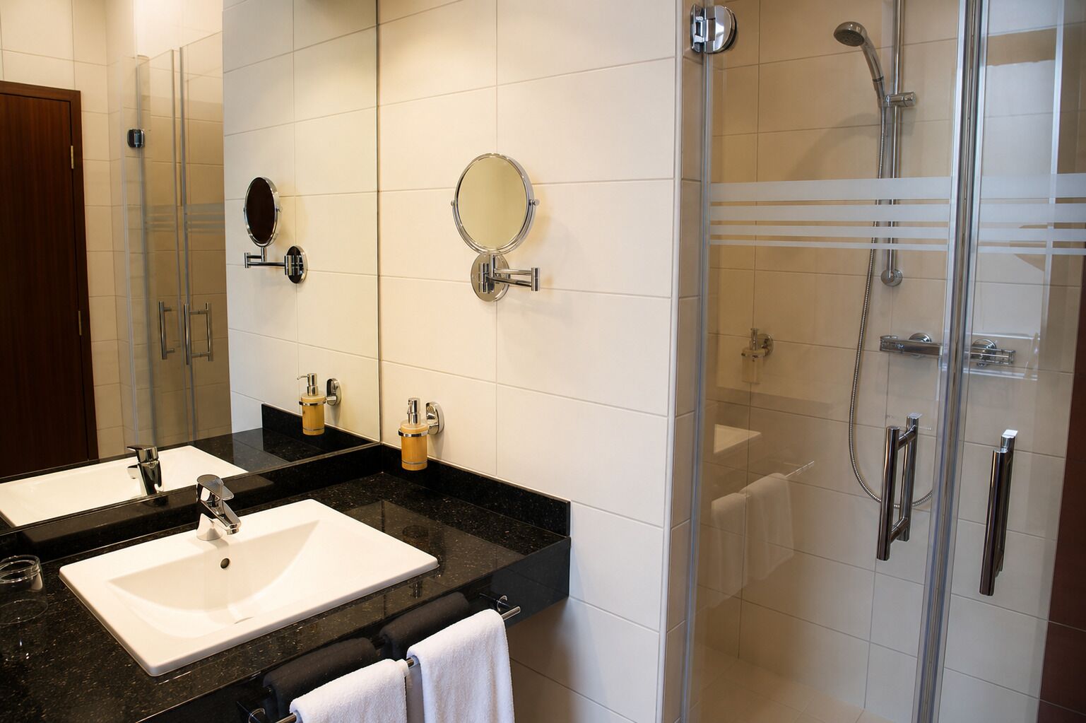 Ein modernes Badezimmer mit einem Doppelwaschbecken, einer Duschkabine aus Glas und einem großen Spiegel.
