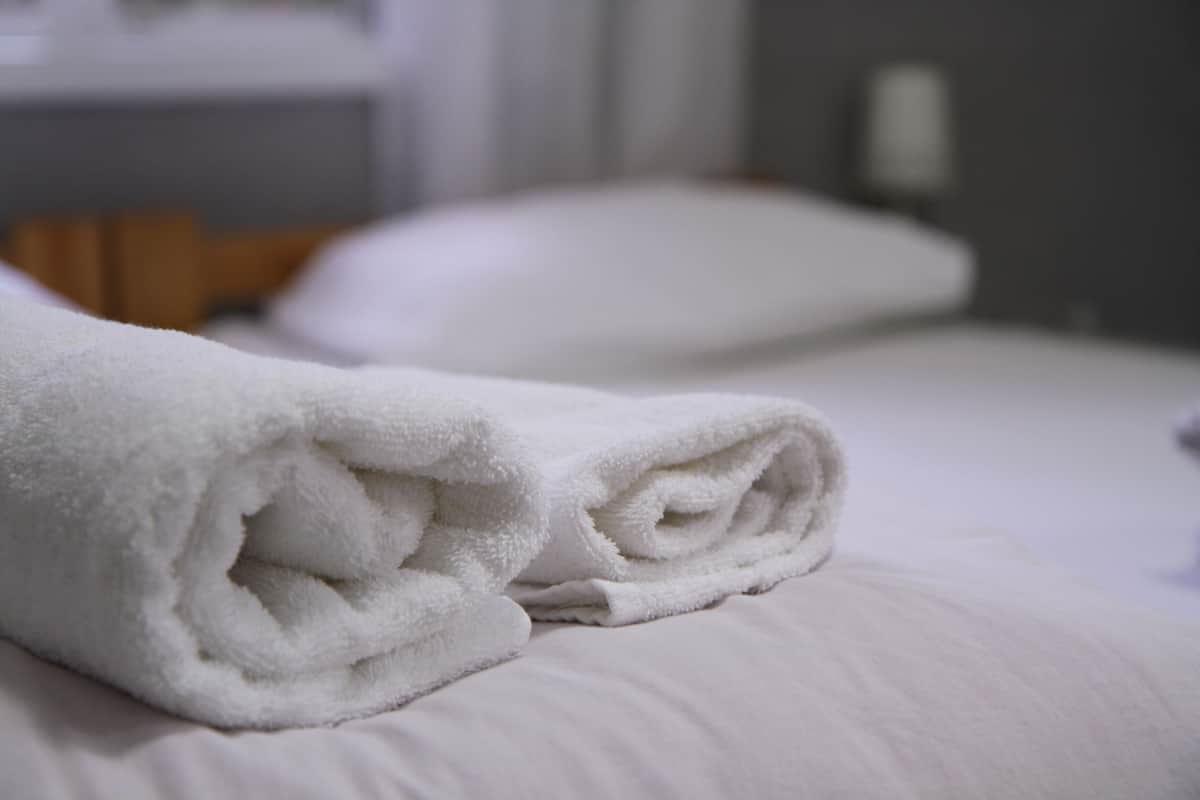 Una toalla blanca doblada con cuidado sobre una cama con un almohadón.