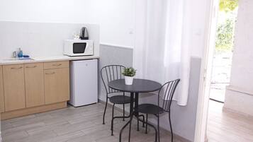 A compact kitchen with a microwave, a small refrigerator, wooden cabinets, a dining table with two chairs, and a potted plant.