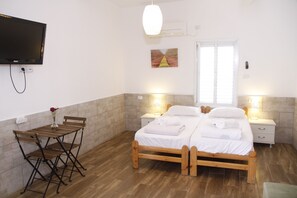 Quarto com duas camas, televisão, mesa com cadeiras e um quadro na parede.