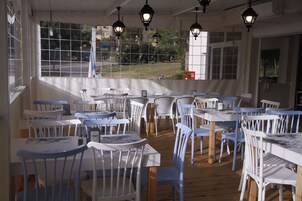Um restaurante com cadeiras e mesas brancas e azuis, piso de madeira e lanternas penduradas.