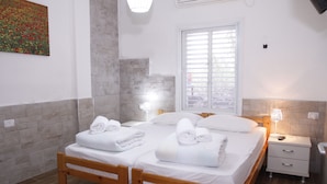 A double bed with two sets of towels, a bedside table with a lamp, and a window with blinds. - Kibbutz Beit Alfa Guest House (Gilboa)