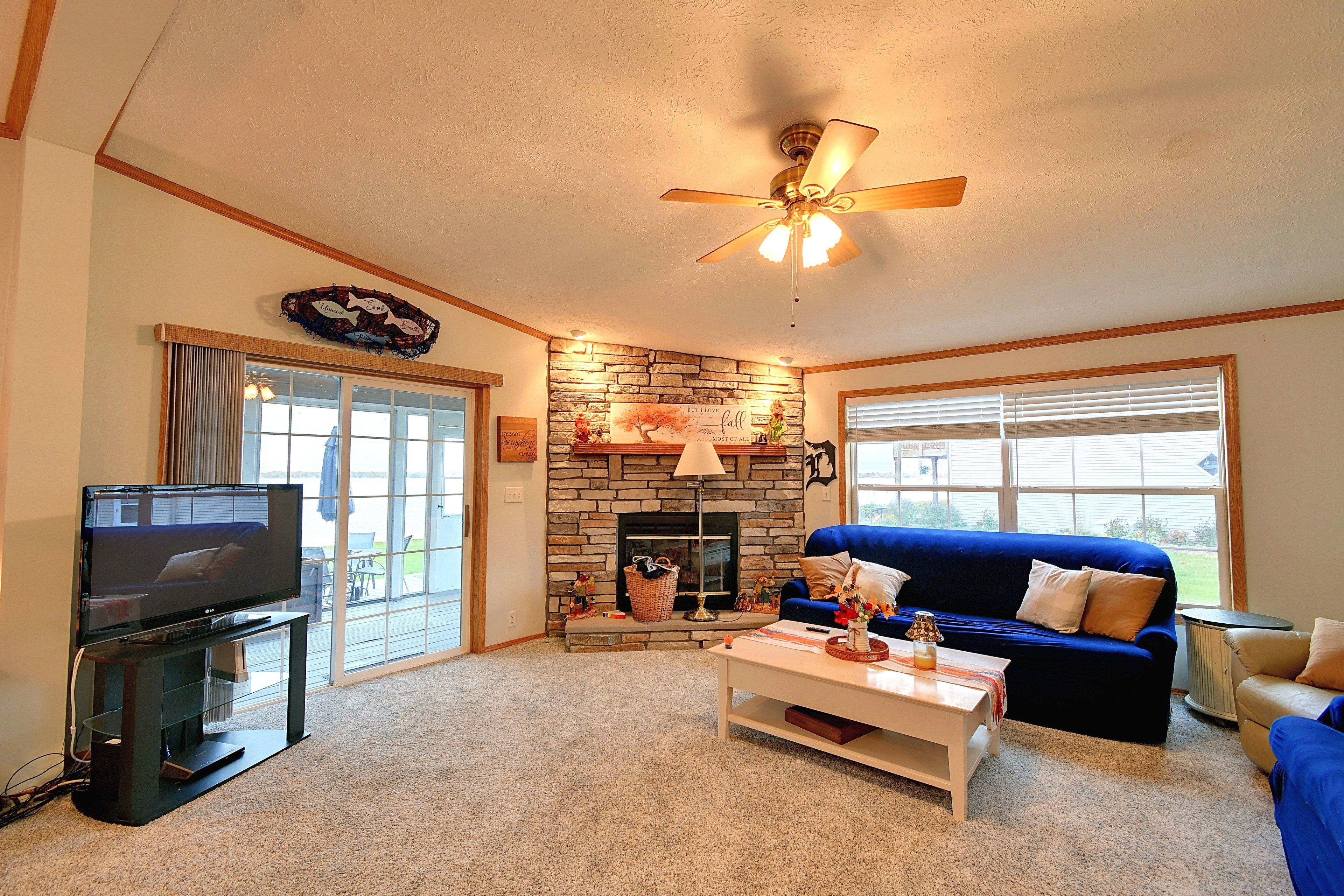 A living room with a television, a stone fireplace, a blue sofa, and a ceiling fan.