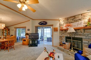 A cozy living room with a fireplace, a dining area with a wooden table and chairs, and a television. - Waterfront Escape on Houghton Lake: Fish & Hike! (Houghton Lake)