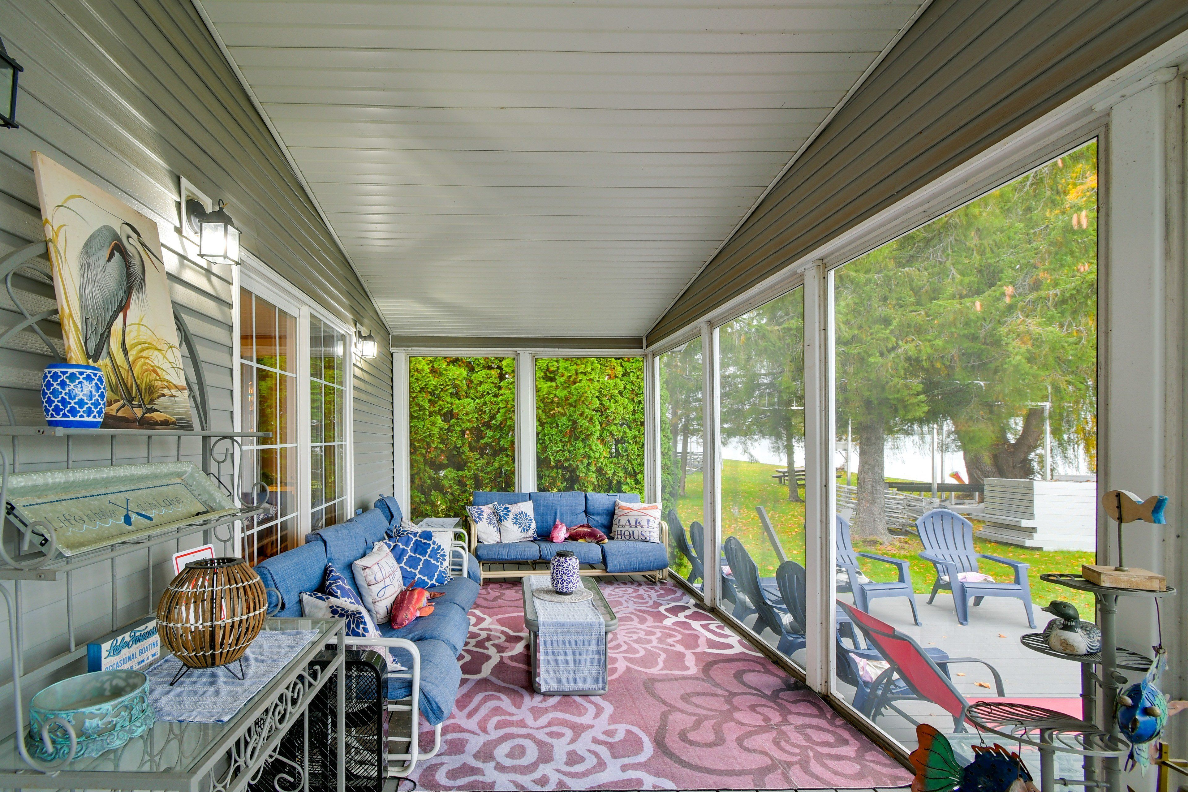 A covered porch with a seating area, a decorative bird painting, and a view of a lake.
