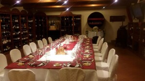 A long dining table set for a formal meal with white chairs, surrounded by wine racks. - Hotel Alla Busa (Noventa Vicentina)