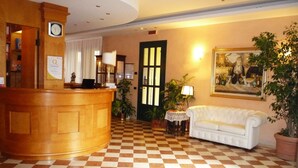 A hotel lobby with a checkered floor, a reception desk, a white sofa, and a door with vertical glass panels. - Hotel Alla Busa (Noventa Vicentina)
