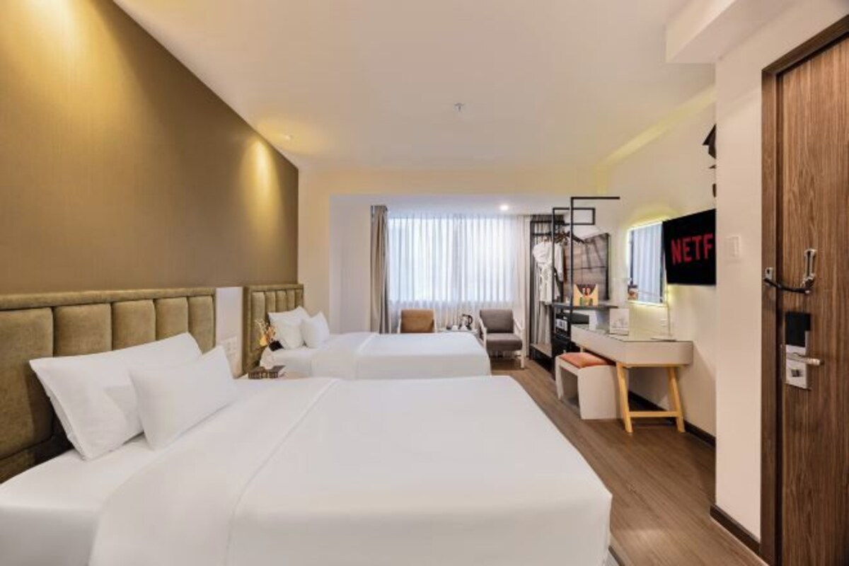 Habitación de hotel con dos camas, un escritorio, una silla, un televisor y una puerta.