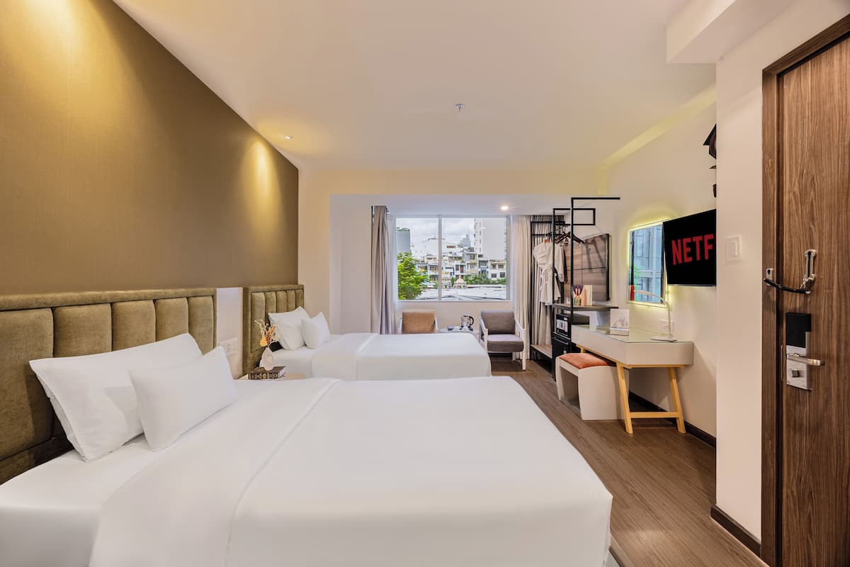 A hotel room with two beds, a desk, a chair, a TV, and a view of the city.