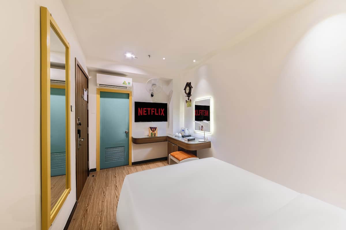 A hotel room with a bed, a desk, a chair, a mirror, a clock, and a sign that says "NETFLIX".