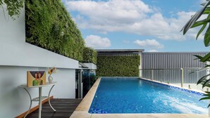 A modern outdoor swimming pool with a wooden deck, surrounded by lush greenery and a clear blue sky. - A25 Premium Hotel - 55 Le Anh Xuan (Ho Chi Minh City)