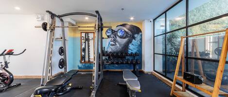 Ein Fitnessraum mit Trainingsgeräten, einer Bank und einer Wand mit Wandgemälde.