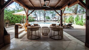A covered outdoor area with a pool, wicker furniture, and umbrellas. - The Gili Beach Resort, 4 Bedrooms Villa Gili Trawangan  - Beach Front (Gili Trawangan)