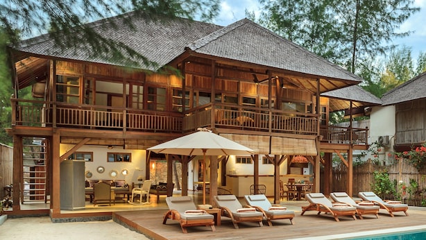 A two-story wooden house with a pool, lounge chairs, and a covered patio area. - The Gili Beach Resort, 4 Bedrooms Villa Gili Trawangan  - Beach Front (Gili Trawangan)