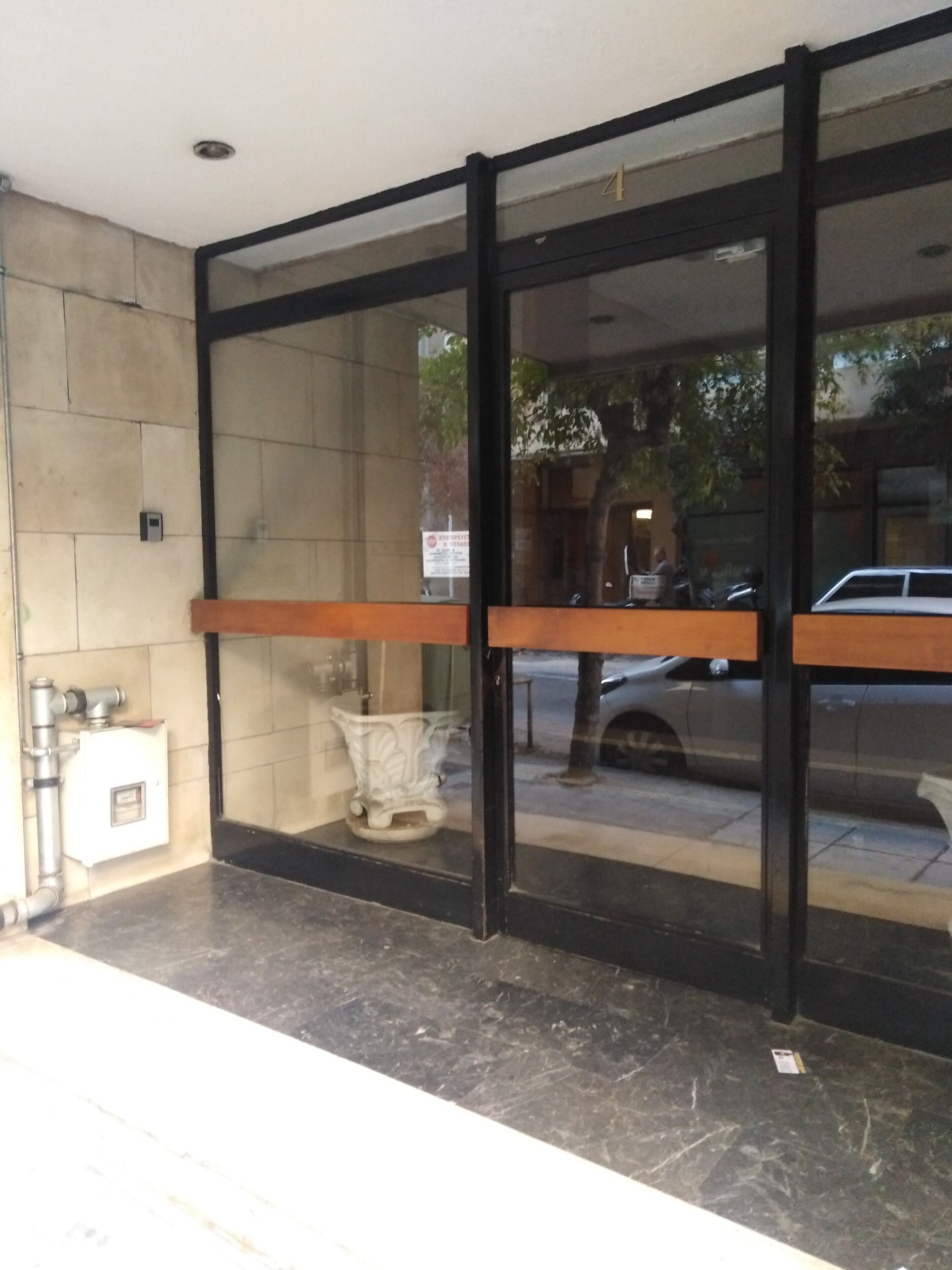A building entrance with a glass door, a bench outside, and a car parked on the street.