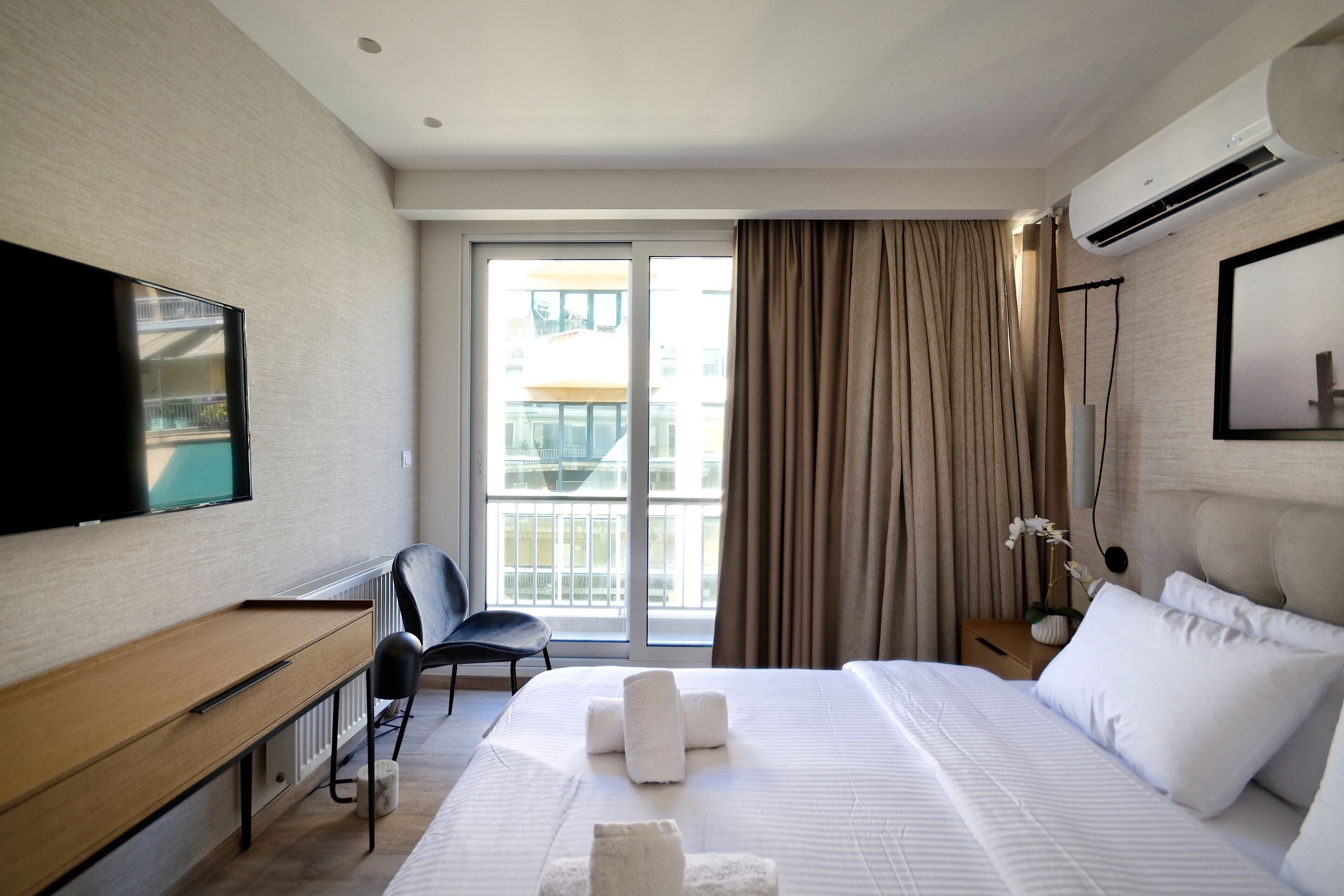 A hotel room with a bed, a TV, a desk, a chair, a nightstand, and a window with curtains.