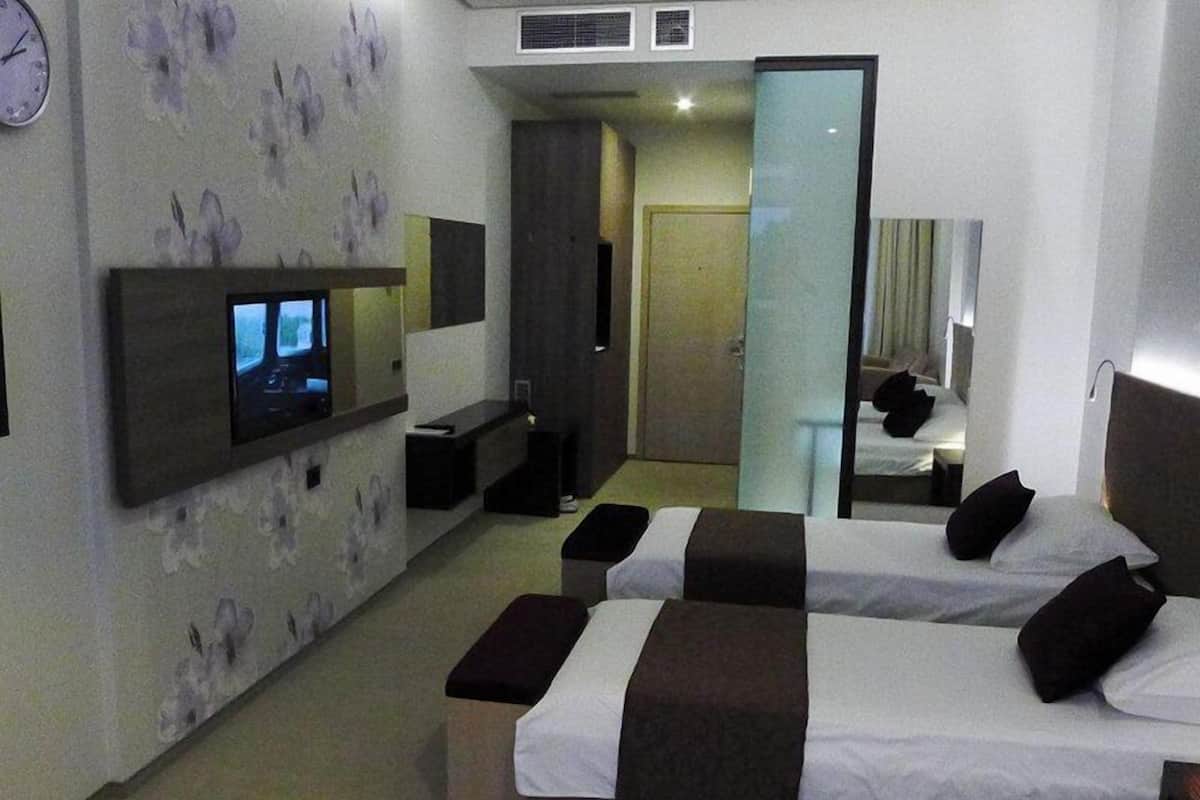 A modern hotel room with a large bed, a TV mounted on the wall, a mirror, and a small seating area.