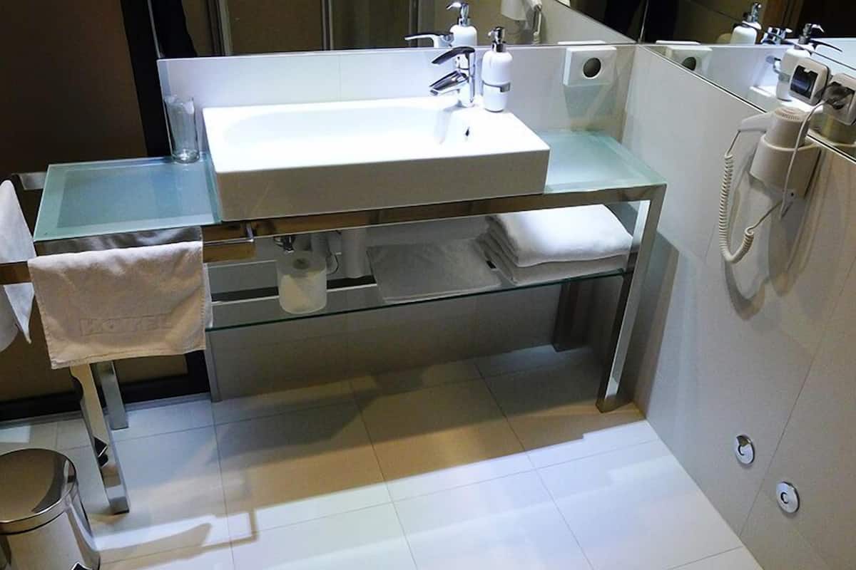 A modern bathroom with a glass-enclosed sink, a towel rack, a toilet, and a hand dryer.
