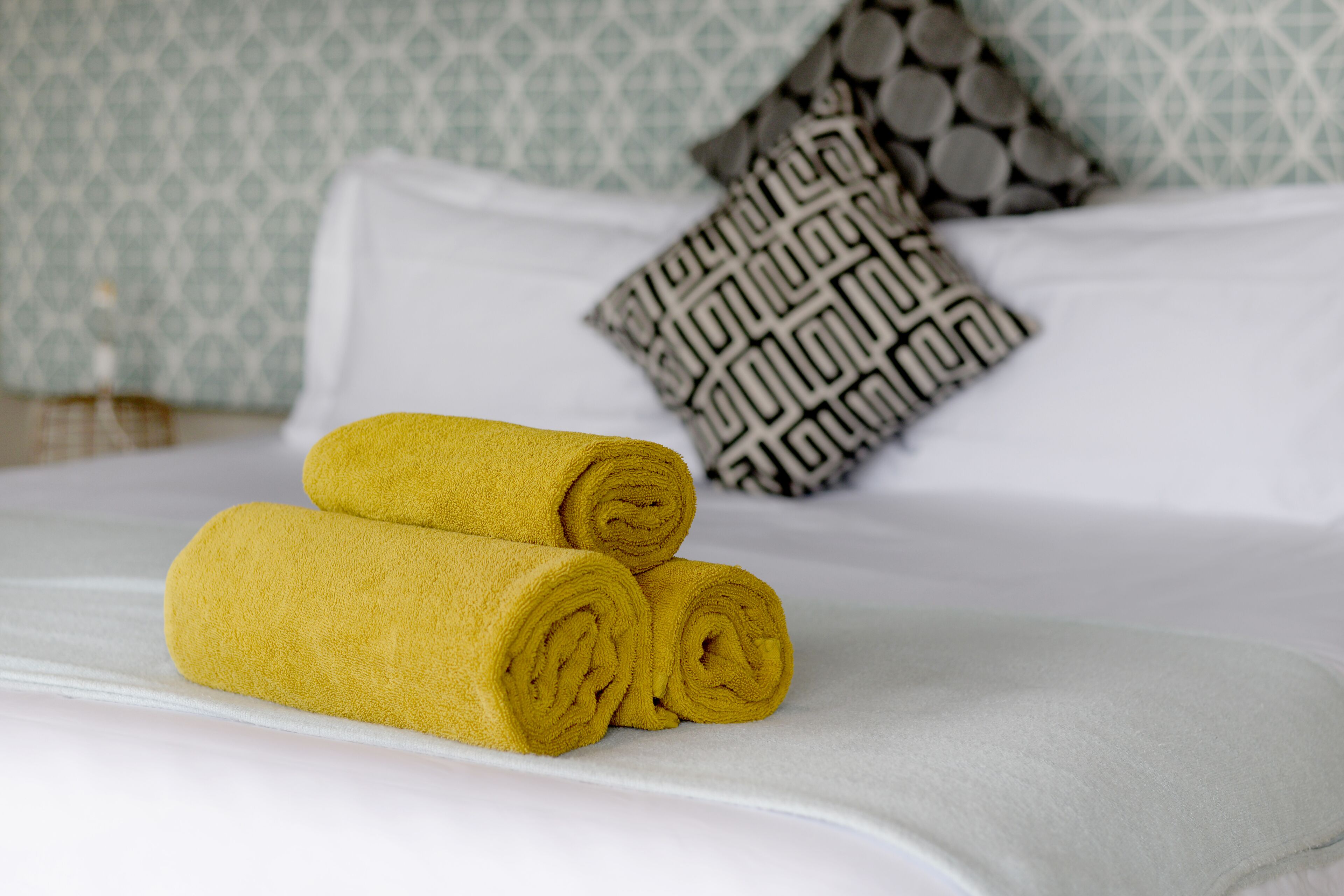 A neatly made bed with rolled yellow towels and a patterned pillow.