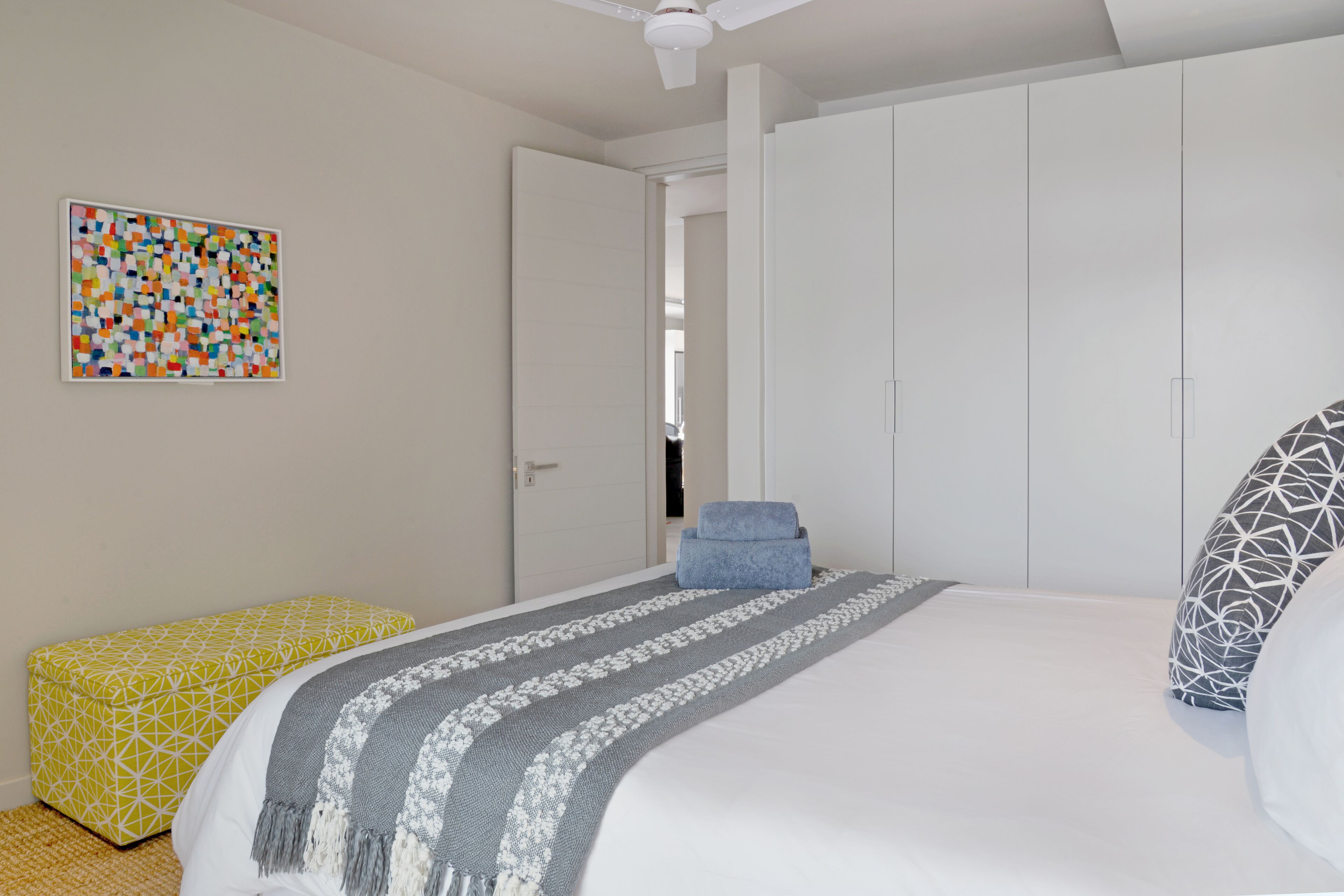 Een slaapkamer met een bed, een kledingkast, een bankje en een kleurrijk abstract schilderij.