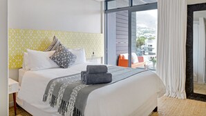 A modern hotel room with a large bed, a view of the city, and a balcony with a table and chairs. - Emily By Stay Amazing (Cape Town)