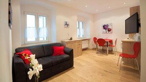 Een moderne woonkamer met een zwarte bank, rode kussens, een salontafel en een eethoek met rode stoelen.