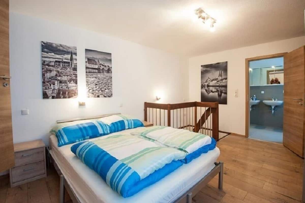 Ein Schlafzimmer mit Bett, Nachttisch, Holz-Kopfstück und zwei schwarz-weißen Stadtbildern an der Wand.