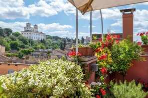 Un balcon agrémenté de plantes et de fleurs en pot, d’où l’on peut admirer un panorama sur la ville, avec ses bâtiments historiques.