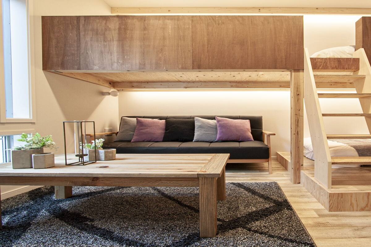 Une chambre de style « loft » avec un lit superposé, un canapé, une table basse et un escalier.