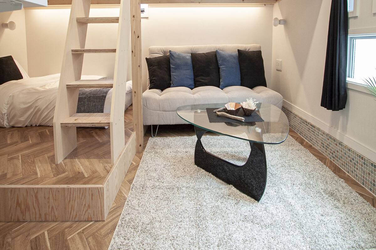 Une chambre moderne de style loft, avec un lit en mezzanine, une table basse en verre et un canapé agrémenté de coussins.