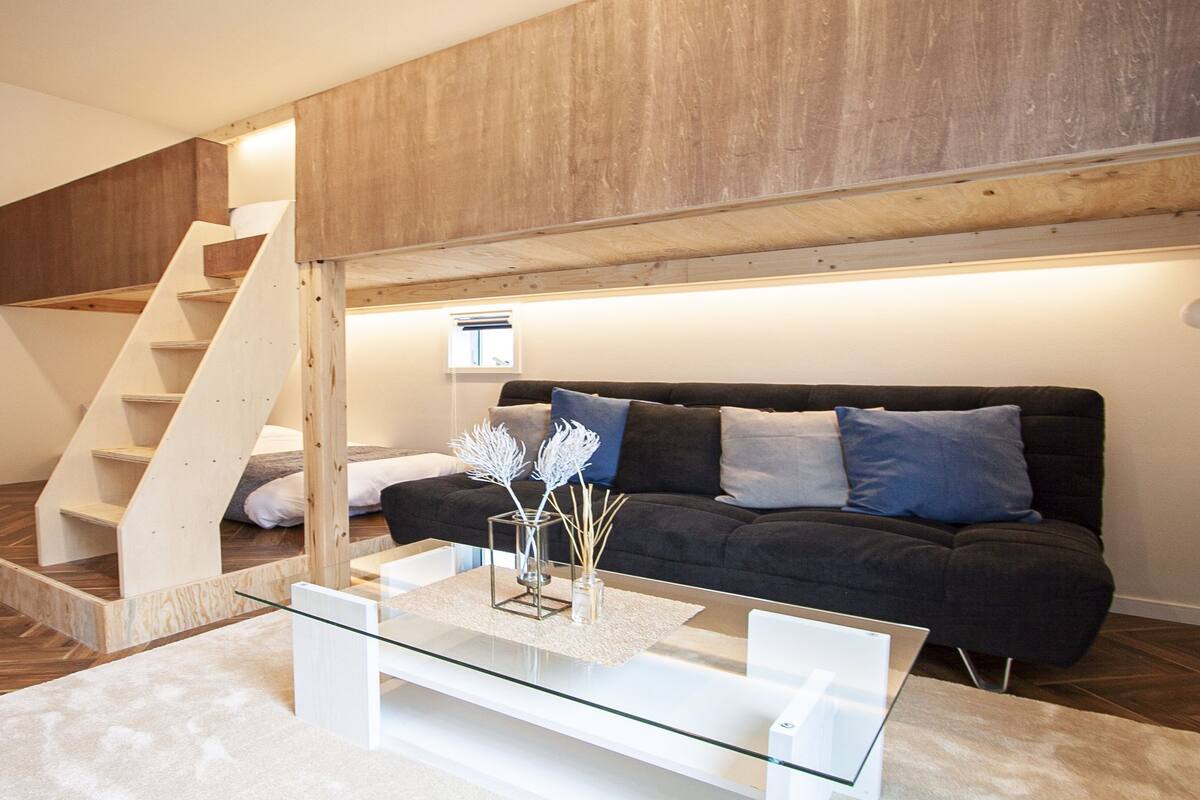 Un salon moderne avec une table basse en verre, un canapé foncé et un escalier en bois.
