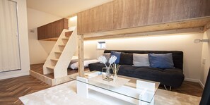 A modern living room with a glass coffee table, a dark sofa, and a wooden staircase. - Grand Cave Yokohama (Yokohama)