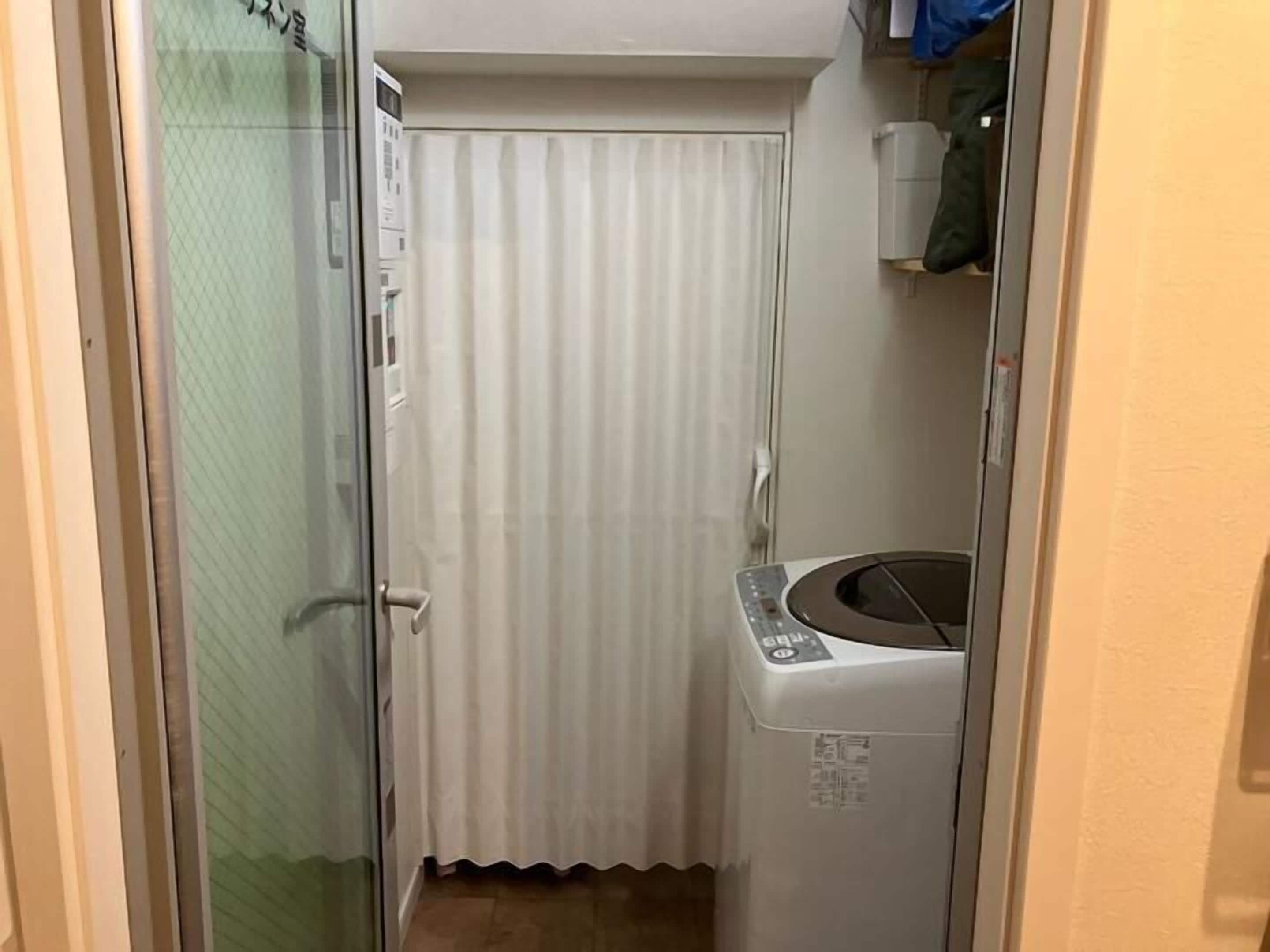 Un baño pequeño con mampara de vidrio, cortina blanca y lavadora.