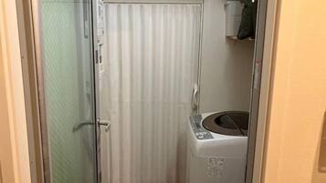 Un baño pequeño con mampara de vidrio, cortina blanca y lavadora.