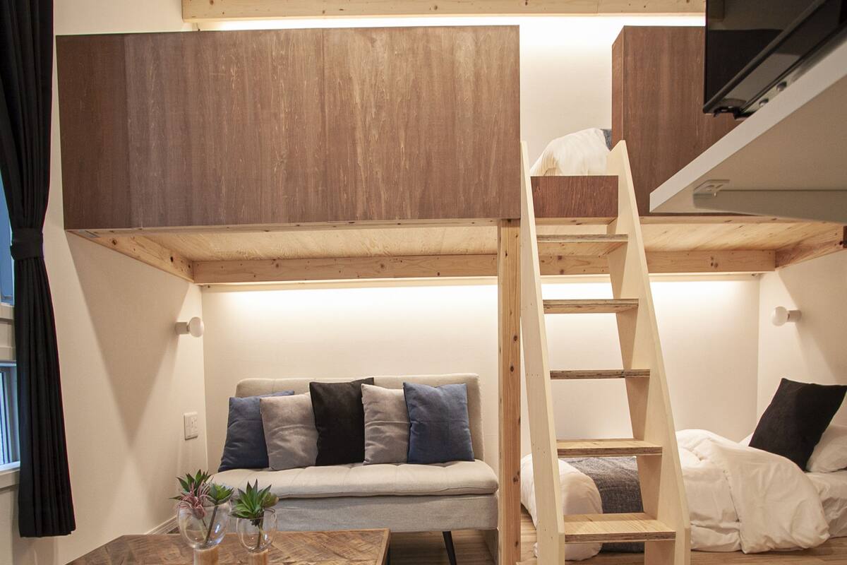 Une chambre à coucher aménagée dans un espace en hauteur, avec un lit superposé, un canapé, une table basse et un escalier.