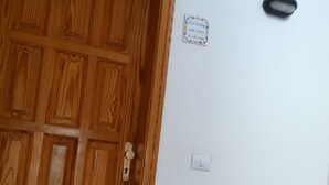 Een houten deur met een slot, een lichtschakelaar en een klein bord aan de muur.